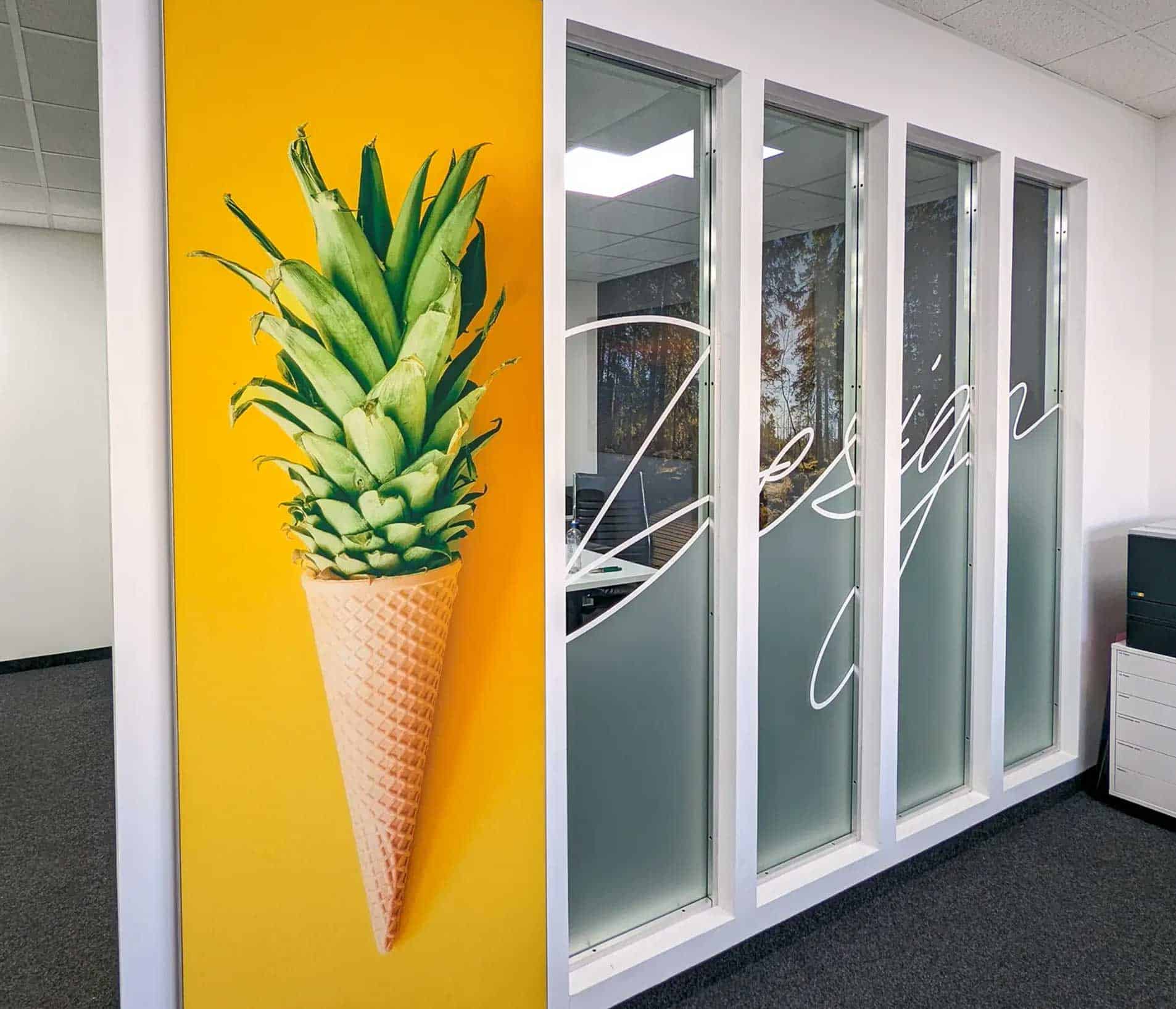 Vier hohe Glaselemente als Abtrennung zu Büroraum - beklebt mit geschwungen geschriebenen "Design" und teilweise Milchglasfolie als Sichtschutz.