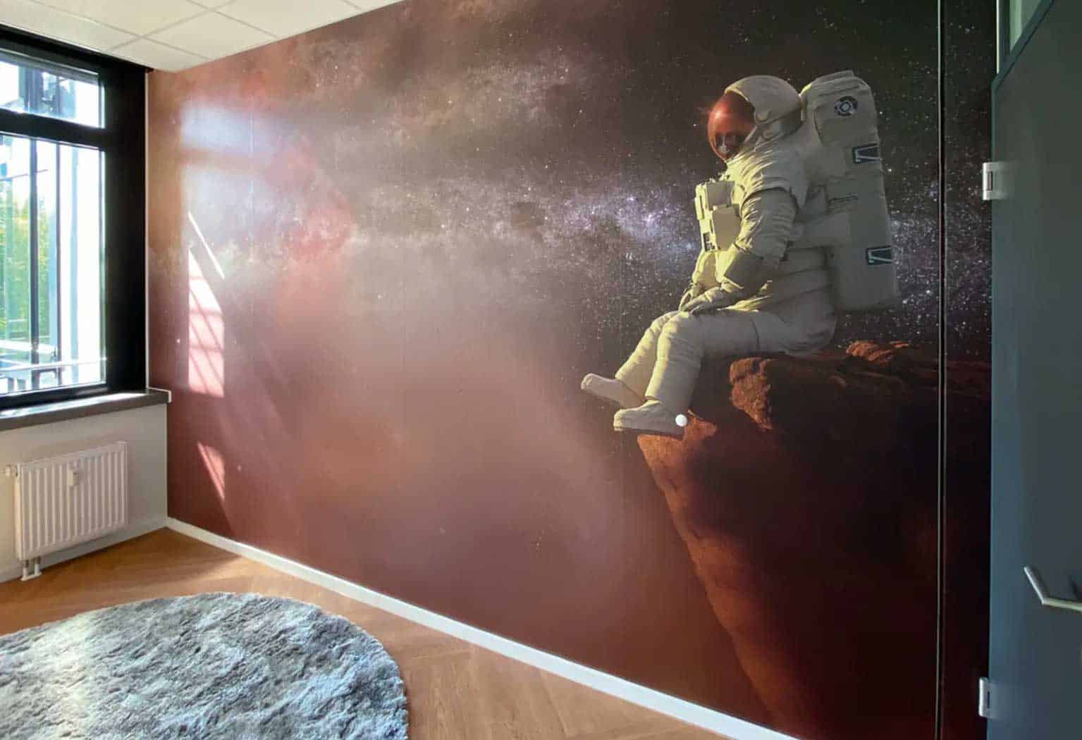 Vollflächige Beklebung einer Wand mit Weltraummotiv und auf einem Fels sitzendem Astronautem.